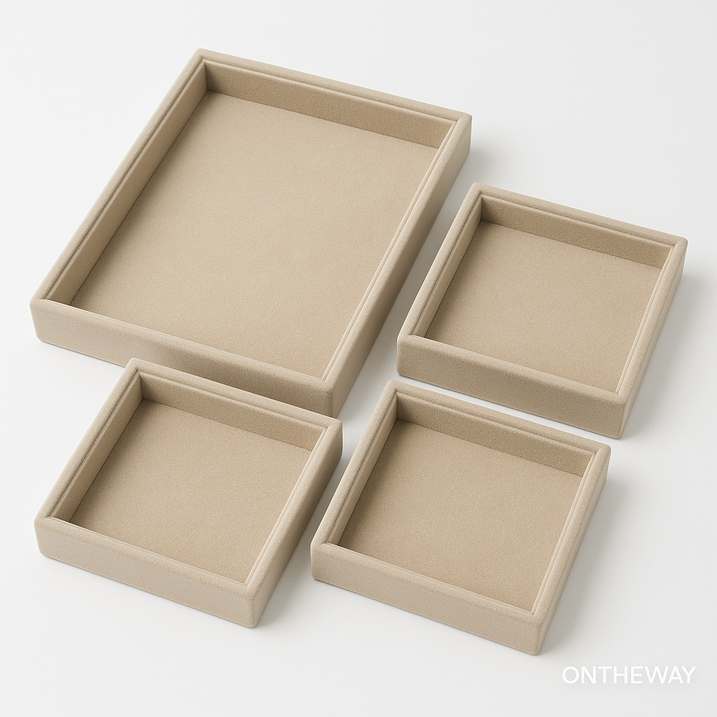 A clean product photo featuring four custom size jewelry trays in different square and rectangular dimensions, arranged in a stepped layout on a white background. The beige velvet finish highlights how custom tray sizes can be tailored for retail counters, wholesale showrooms, exhibitions, and storage systems. A subtle ONTHEWAY watermark appears in the bottom right corner.